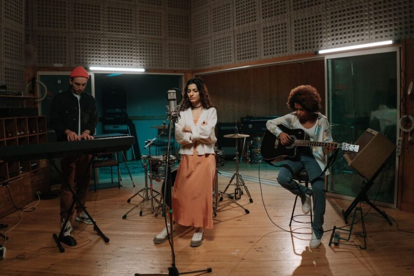 Drie muzikanten repeteren in een geluidsstudio met keyboard, microfoon en gitaar
